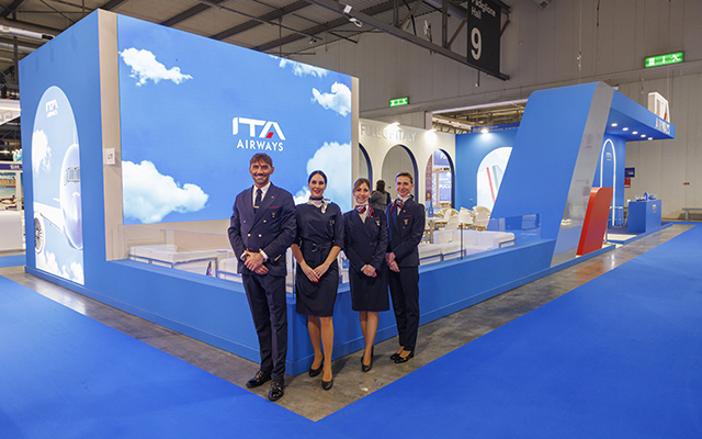 ITA Airways a group of people in uniform standing in front of a blue display